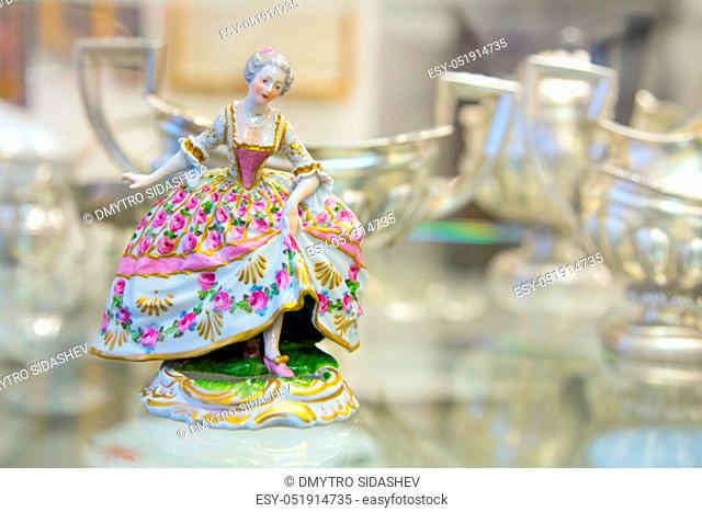 Color vintage porcelain doll in the blurry background. The doll depicts a medieval lady in a ball gown. Porcelain doll in vintage interior