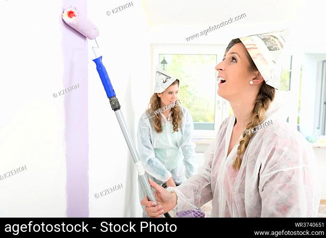 Female worker wearing paper hat painting the wall with roller