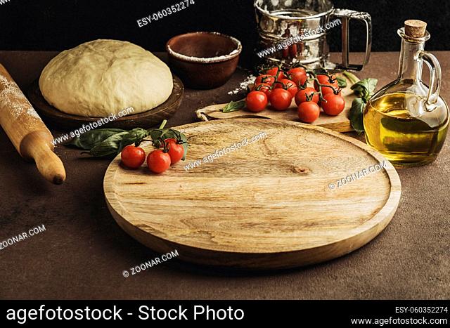 high angle of pizza dough with wooden board and tomatoes