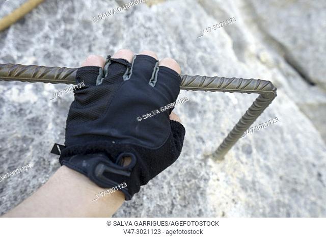 Hand of a man with climbing gloves holding on an iron bar of a via ferrata