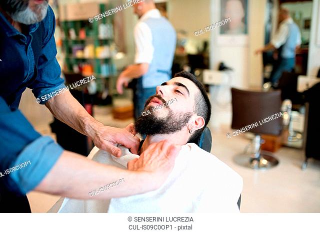 Hairdresser preparing to shave customer's beard in barber shop