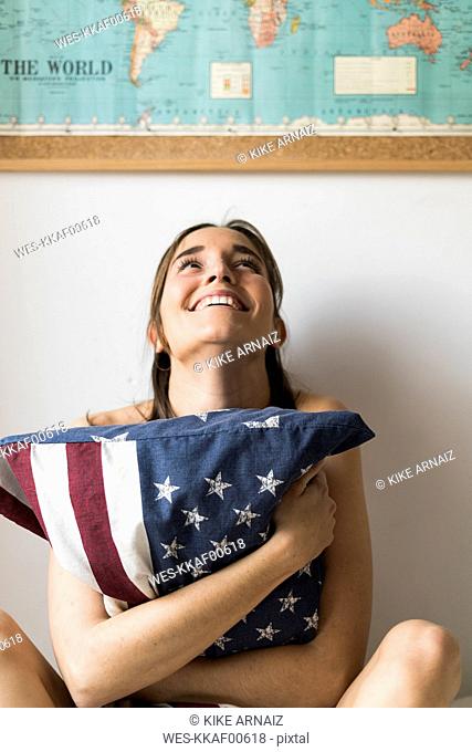 Smiling young woman holding US cushion under world map
