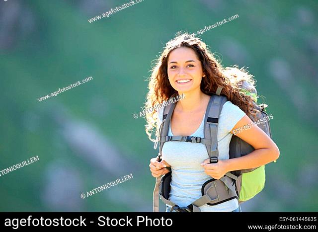 Happy hiker wearing backpack posing looking at you in the mountain