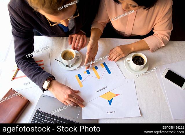 Top view image of two managers working with papers and data. Having coffee while working