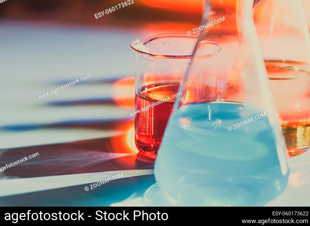Illuminated laboratory flask filed with colorful chemical solutions with shadows on the table. Laboratory, science, reaserch, chemistry... consept