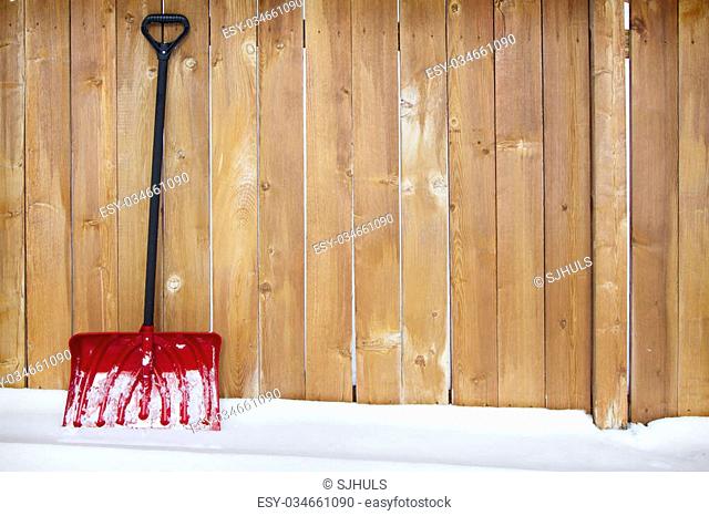 Red snow shovel leaning up against a fence on a snow drift