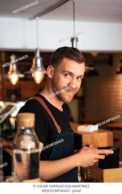 Portrait of smiling barista using mobile phone in coffee shop