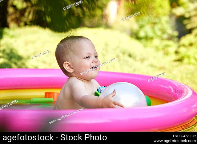 Happy cute baby girl with ball in kid inflatable pool in the garden