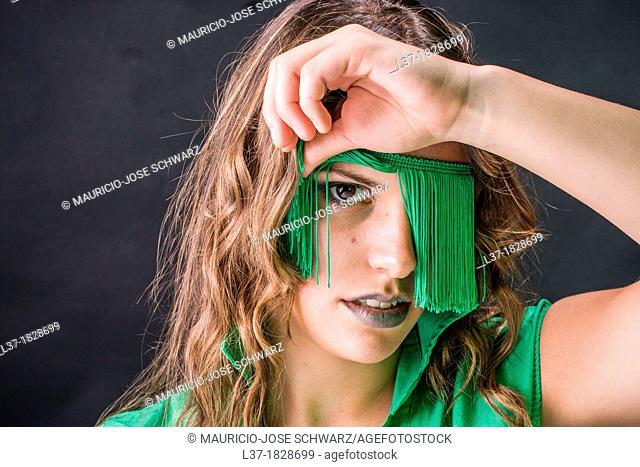 Young woman looking out from a blindfold of green fringes