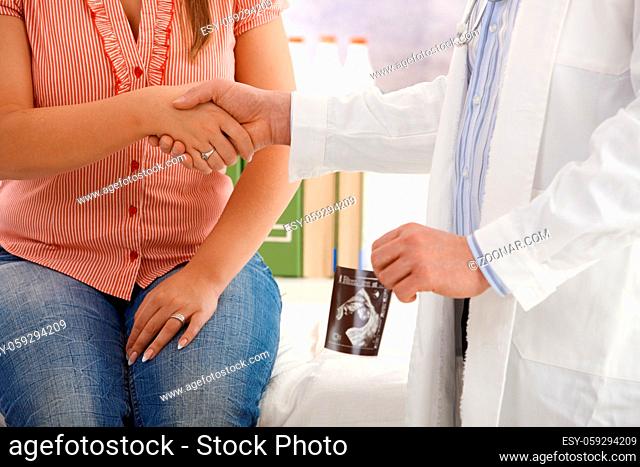 Pregnant woman shaking hands with doctor after consultation, doctor holding ultrasound photo of baby