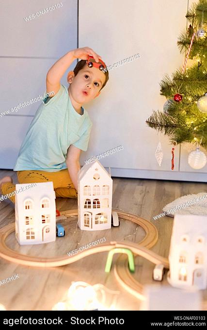 Cute boy playing with miniature train toy near Christmas tree at home