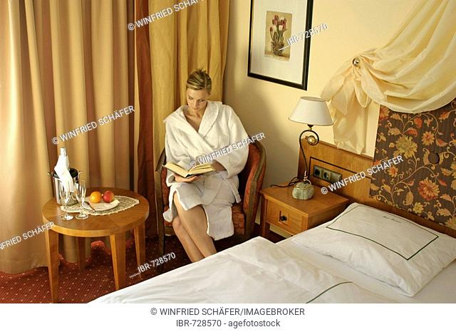 Woman dressed in a bathrobe sitting in a chair reading a book