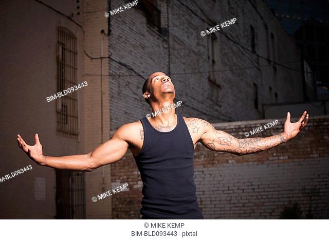 Black man standing outdoors with arms outstretched