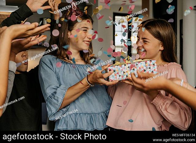 Friends throwing confetti on teenager giving gift to birthday girl in party