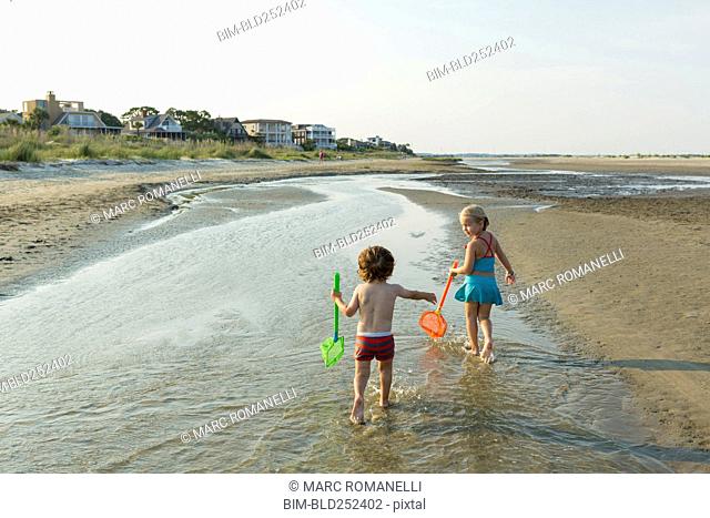 Caucasian brother and sister carrying nets on beach