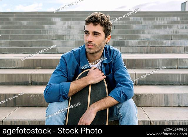 Young man with skateboard sitting on steps