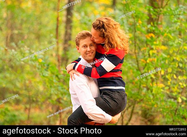 Man lovingly picks up woman in the woods. Arms around each other. in half body