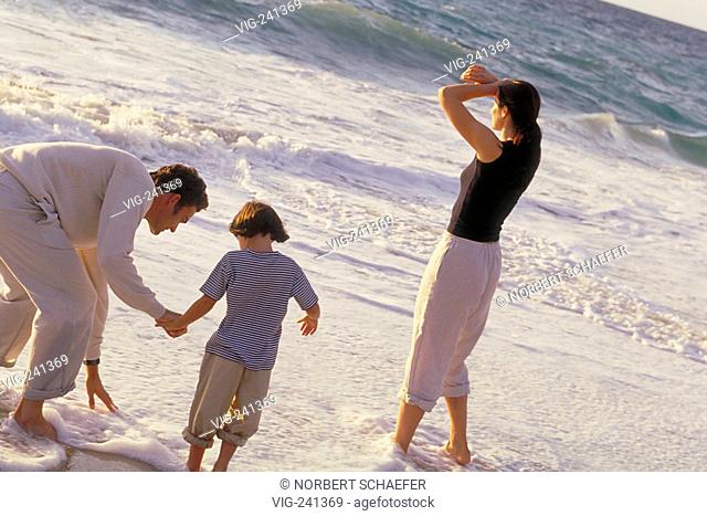 beach-scene, full-figure, dark-haired family with 4 year old daughter is playing bare feeted in the shallow water, all are wearing khaki trousers  - GERMANY