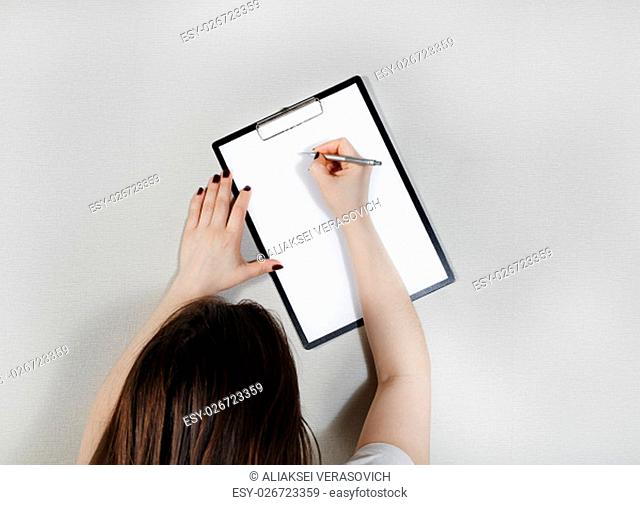 Clipboard with blank paper in female hands. Woman writes on blank white sheet of paper