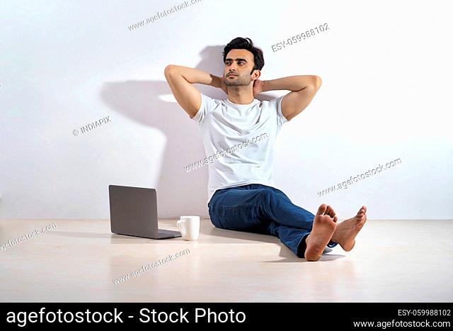 A young man sitting on floor with a laptop and coffee mug beside