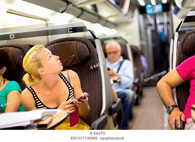 Thoughtful young lady surfing online on smartphone while traveling by train