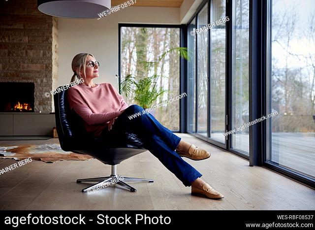 Woman looking through glass window sitting on chair in living room