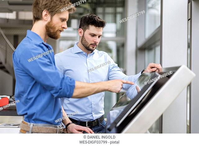 Two businessmen in company using touchscreen