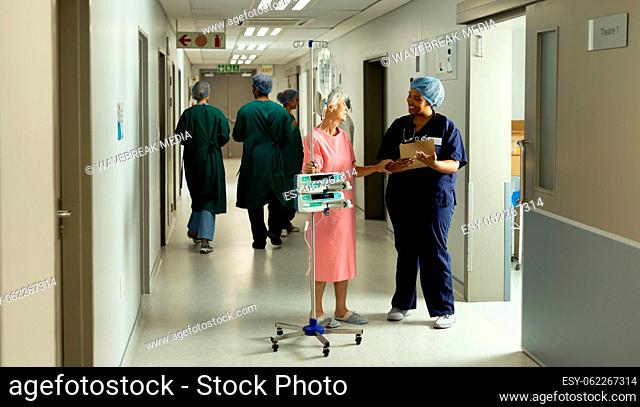 Diverse female doctor and caucasian senior female patient with iv pole talking in hospital