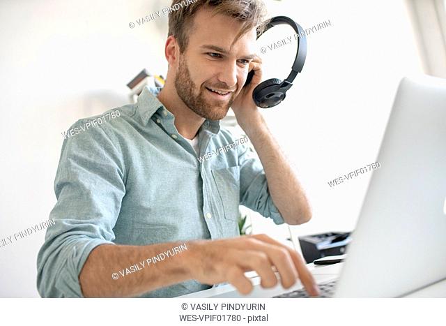 Smiling man with headphones and laptop at desk in office