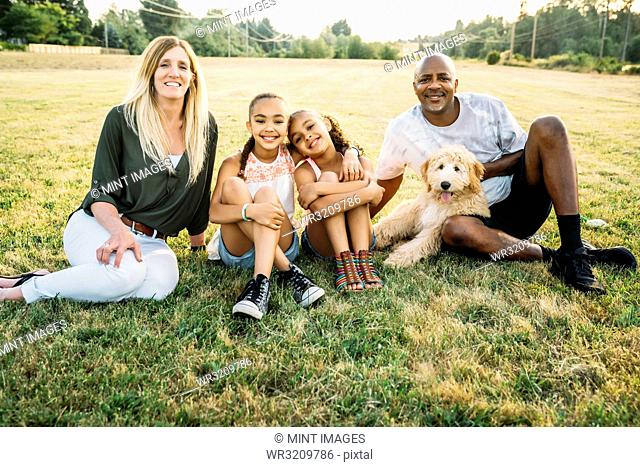 Portrait of mixed-race family in field with labradoodle puppy