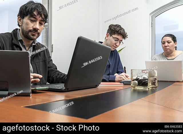 Group of employees sitting around the office meeting table working on their notebooks