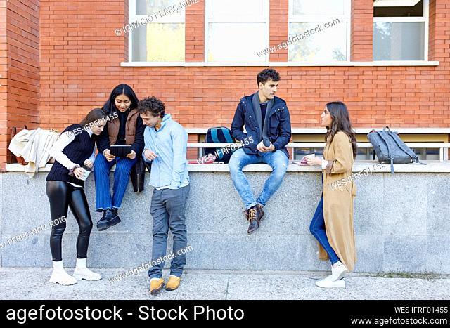 Multiracial students discussing on project by wall on campus