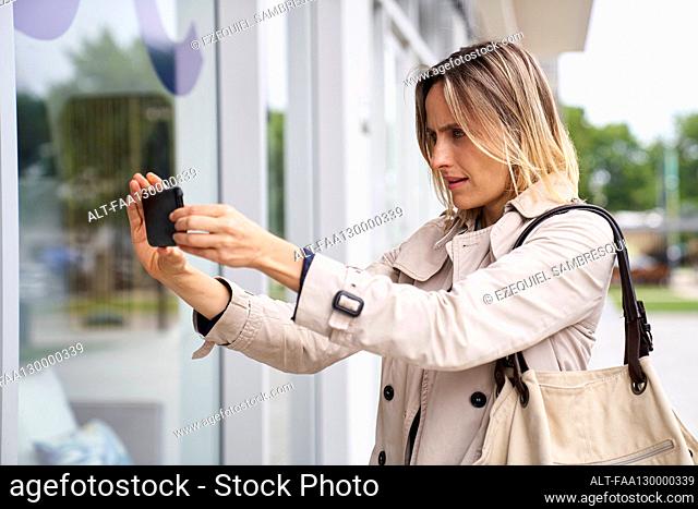 Medium shot of woman taking a photo of shop window with her mobile phone
