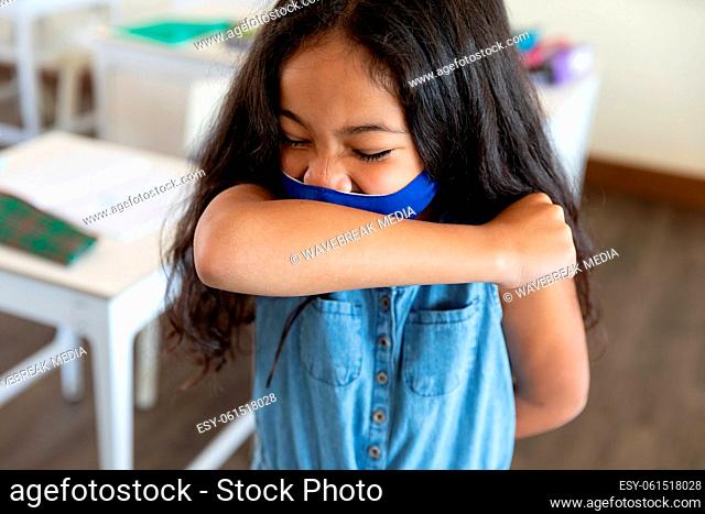 Girl wearing face mask sneezing while covering her mouth at school