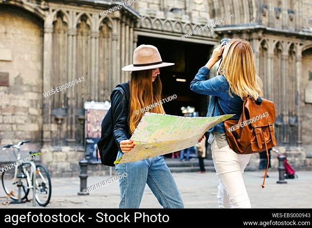 Spain, Barcelona, two young women on square with camera and map