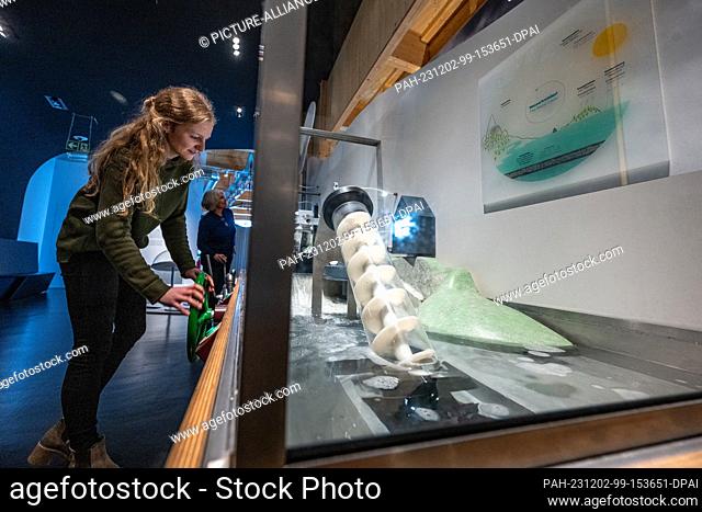PRODUCTION - 30 November 2023, Bavaria, Straubing: Two museum employees stand at the model of a hydroelectric power plant in an exhibition room of the Nawareum