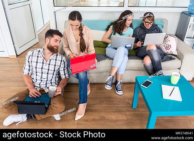 Happy young people laughing while sharing a collaborative office space as co-workers in a modern hub with WI-FI wireless network for digital nomads