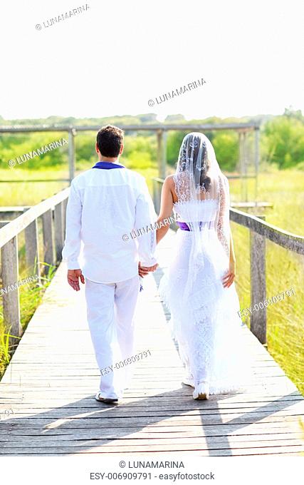 Couple happy in wedding day walking in outdoor rear view