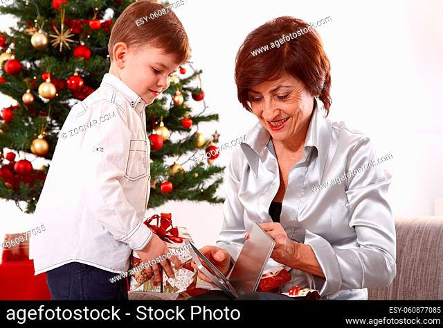 Grandmother and grandson opening christmas presents together, smiling