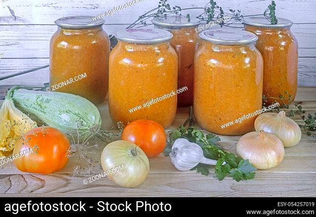 Home preservation of vegetables: glass jars with zucchini caviar with onions, tomatoes, garlic, herbs. With airtight cover made of metal