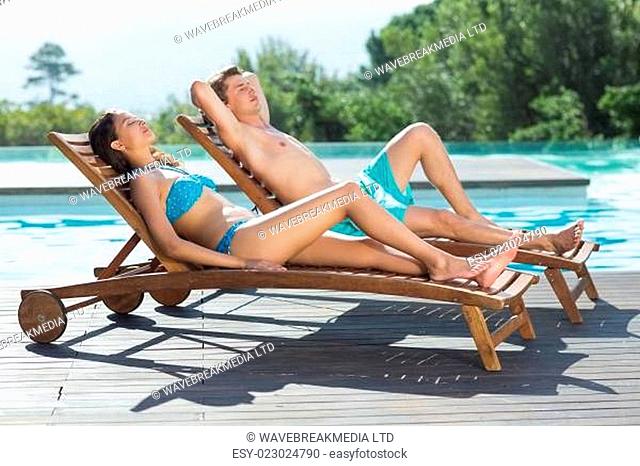 Couple sitting on sun loungers by swimming pool