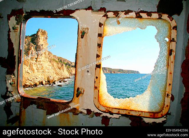 Shipwreck. Rusty abandoned cargo ship near mountain coast. Broken window