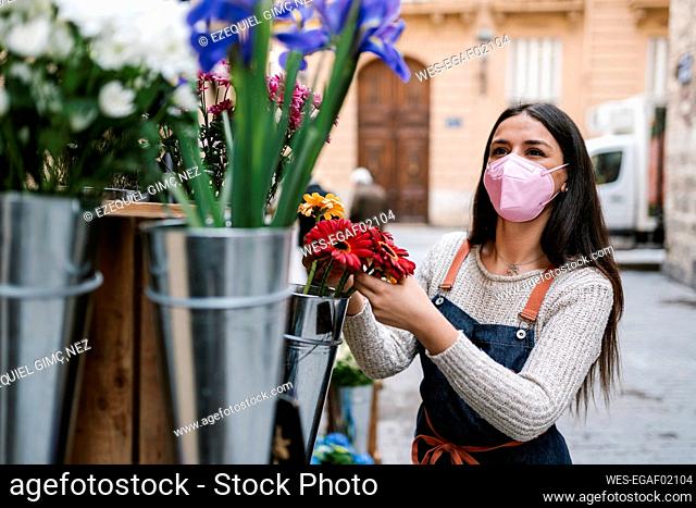 Young female florist with protective face mask looking away while working at flower shop