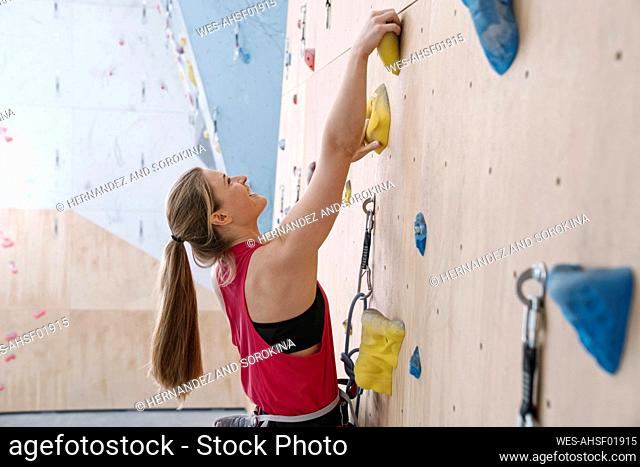 Happy woman climbing on the wall in climbing gym
