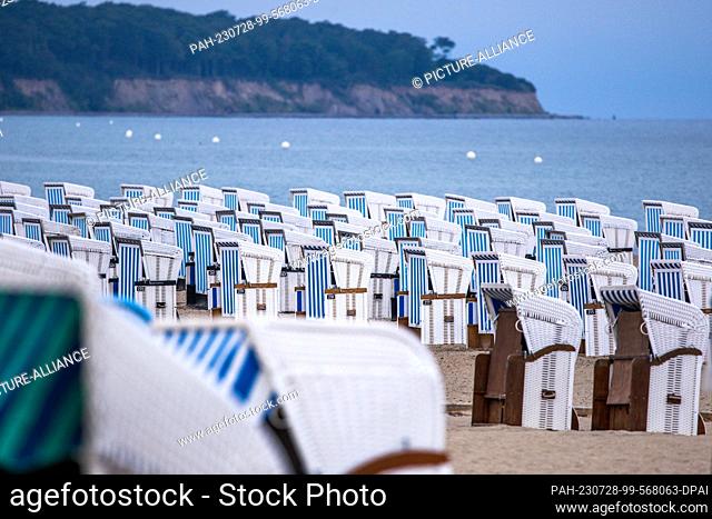 28 July 2023, Mecklenburg-Western Pomerania, Rostock: Empty beach chairs stand in the morning rain on the Baltic Sea coast in Warnemünde