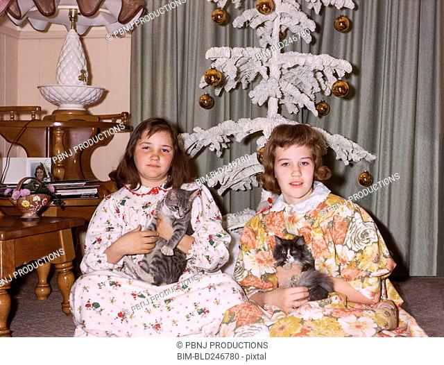 Portrait of Caucasian sisters wearing pajamas holding cats on Christmas