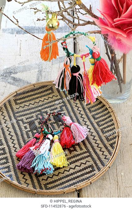 Colourful handmade woollen tassels on a raffia plate and hanging on a twig