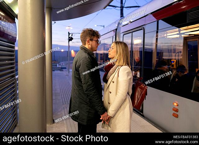 Young couple in love standing at tram stop in the evening looking at each other