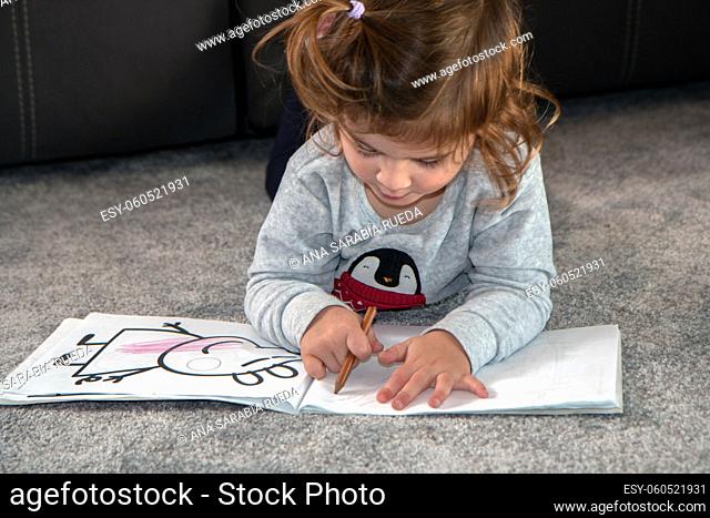 Portrait of innocent girl painting. Schoolgirl sitting on the floor colouring. Girl plays with paints and draws on a sketch pad