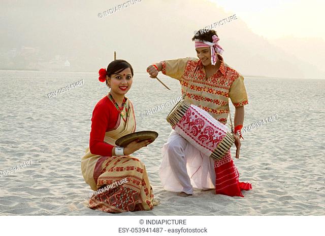 Bihu woman dancing with a brass plate as Bihu man plays on a dhol